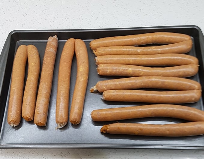 Uncooked sticks of pepperoni on a baking tray.
