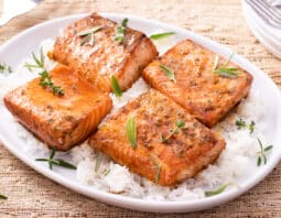 cooked salmon on top of bed of rice garnished with fresh herbs; stack of plates and forks showing in top right corner
