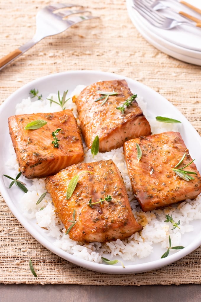 cooked salmon on top of bed of rice garnished with fresh herbs; stack of plates and forks showing in top right corner