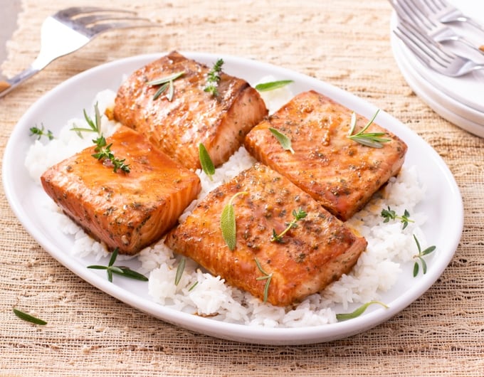 cooked salmon on top of bed of rice garnished with fresh herbs; stack of plates and forks showing in top right corner