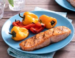 grilled seasoned salmon on light blue plate with grilled baby bell peppers; blue napkin under plate; glasses of water in background