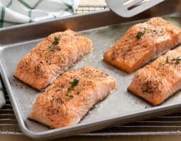 baking sheet with 4 filets of salmon; white cloth with green stripe checked in background