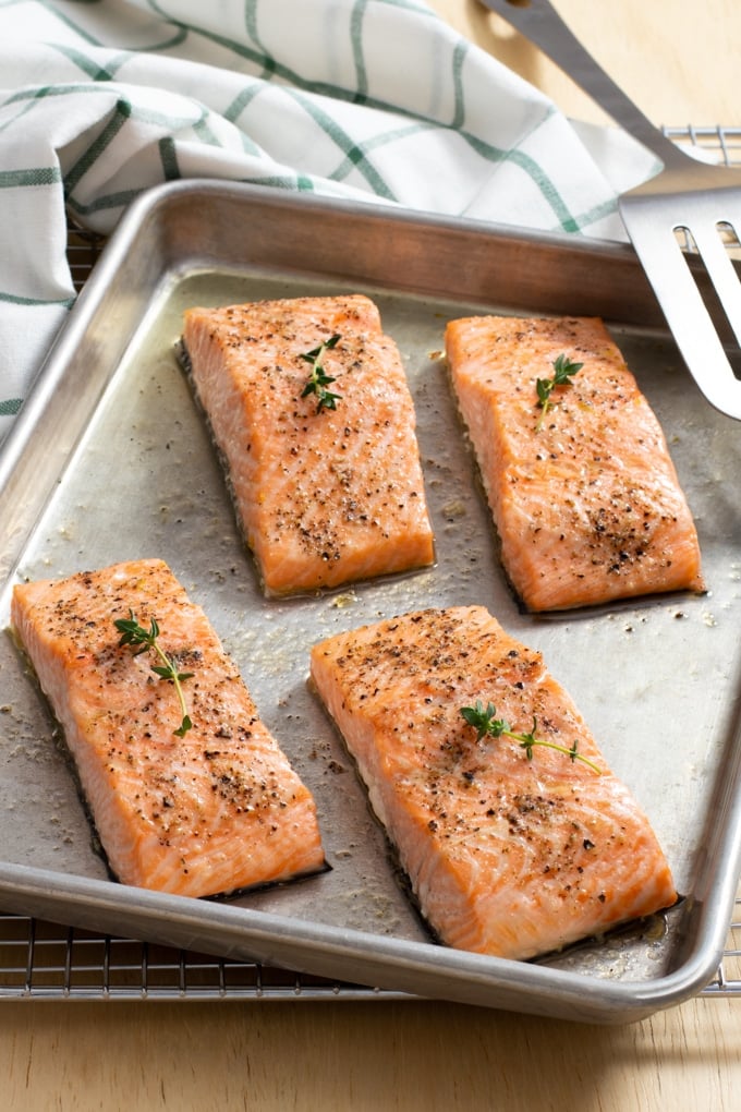 baking sheet with 4 filets of salmon; white cloth with green stripe checked in background