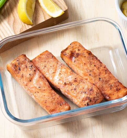 baked salmon filets in glass container with green onion and lemon wedges in background