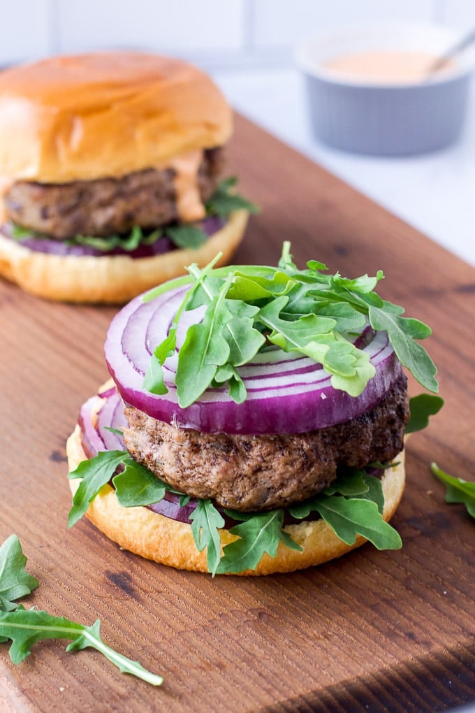 lamb burger on bun with arugula and red onion with another burger in background