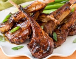 fried lamb lollipops on white platter garnished with slivers of green onion, light green cloth in background
