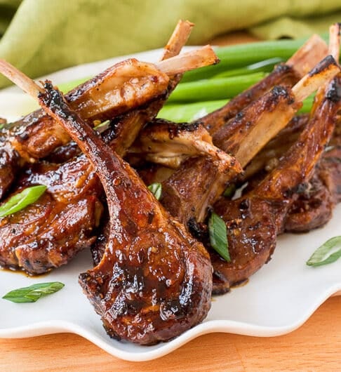 fried lamb lollipops on white platter garnished with slivers of green onion, light green cloth in background