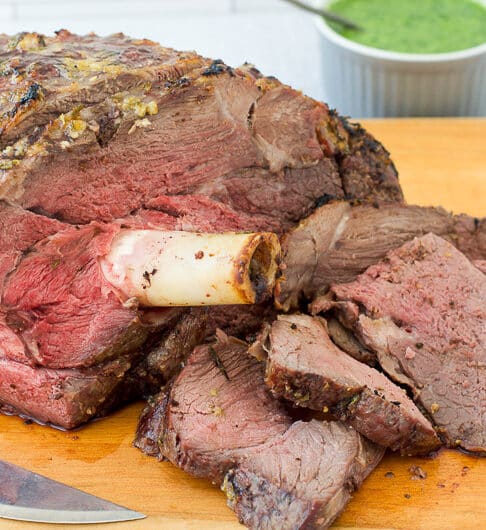 Roasted leg of lamb with slices cut off on cutting board with mint sauce in background