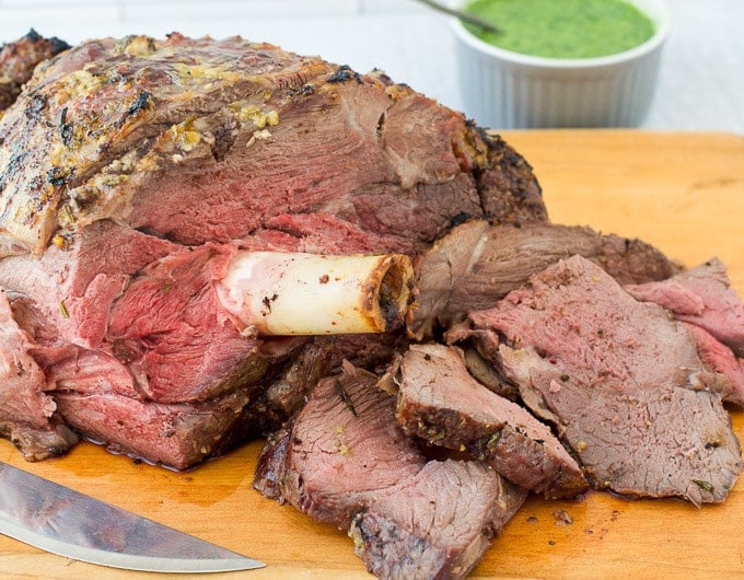 Roasted leg of lamb with slices cut off on cutting board with mint sauce in background