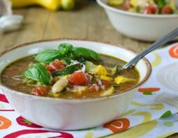 Bowl with brown rim full of summer minestrone soup and topped with fresh basil.