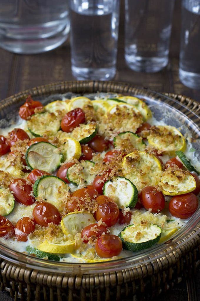 sliced zucchini and cherry tomatoes topped with cream sauce, cheese, and bread crumbs