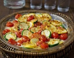 sliced zucchini in a casserole dish with cream sauce and tomatoes. Topped with cherry tomatoes and breadcrumbs.