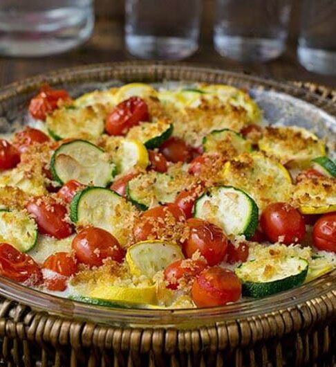 sliced zucchini in a casserole dish with cream sauce and tomatoes. Topped with cherry tomatoes and breadcrumbs.
