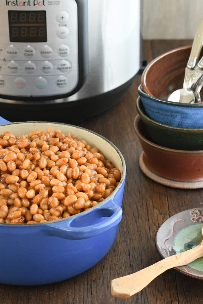 Baked beans in a large blue pot, in front  of bowls and an Instant Pot.