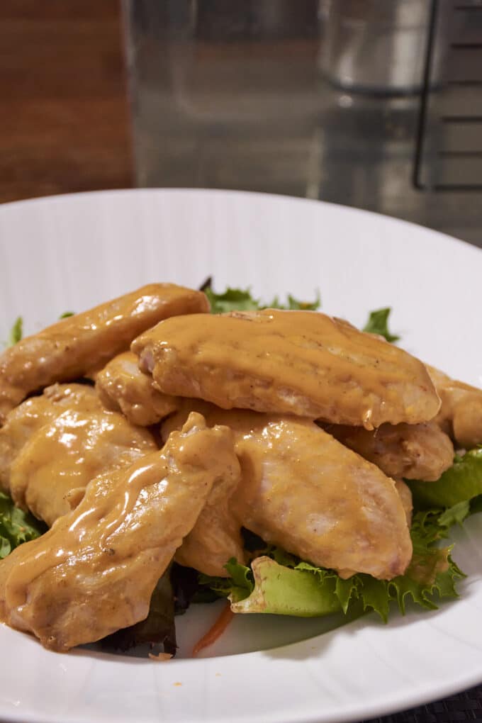 Chicken wings with buffalo sauce on salad greens on a white plate.