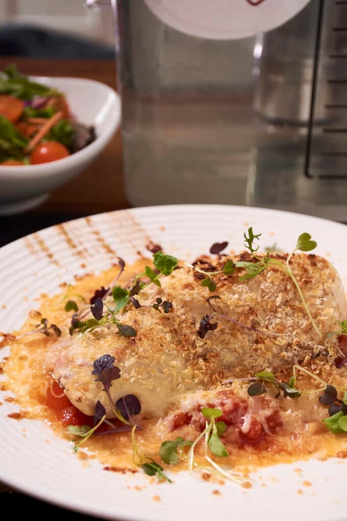 Chicken Parmesan topped with cheese, breadcrumbs, and microgreens on a white plate.