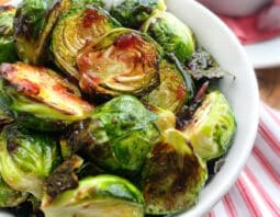 Brussels Sprouts with cranberry glaze in a white bowl, cranberries and sauce in background.
