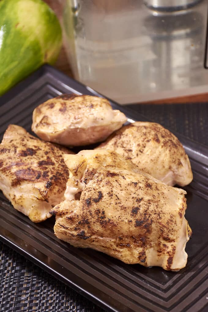 Four chicken thighs on a dark rectangular platter.