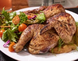 Spatchcock chicken on a white plate with vegetables.