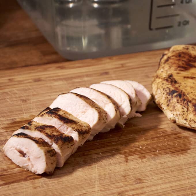 Sliced chicken breast on a wooden cutting board in front of a sous vide water bath.