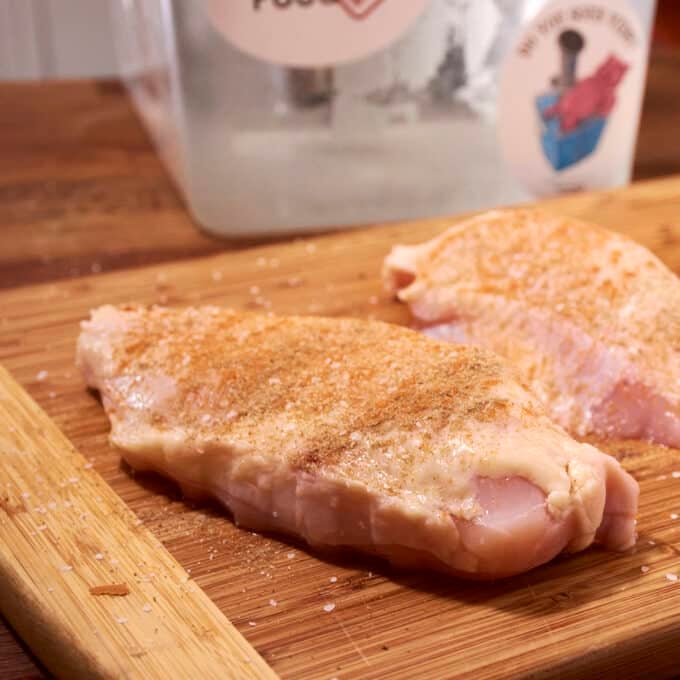 Raw seasoned chicken breasts on a wooden cutting board.