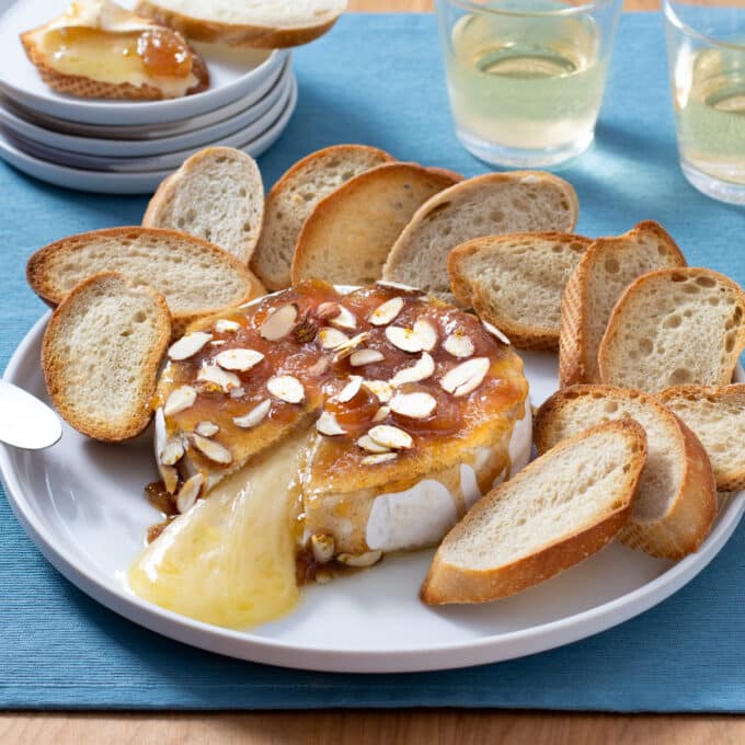 Baked brie wheel with cheese oozing out, bread rounds beside.