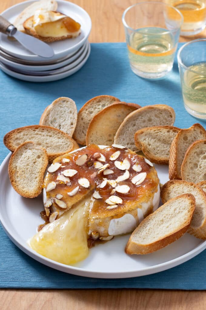 Baked Brie topped with mango chutney and sliced almonds on a white plate with bread.