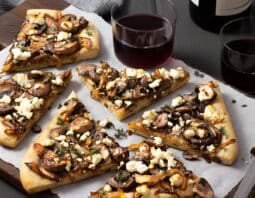 Mushroom pizza with onions and goat cheese on a wooden board with parchment paper.