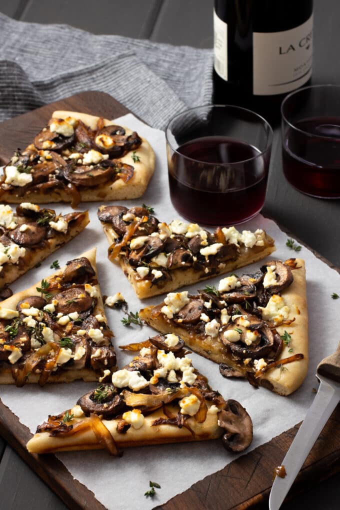 Mushroom pizza with onions and goat cheese on a wooden board with parchment paper.