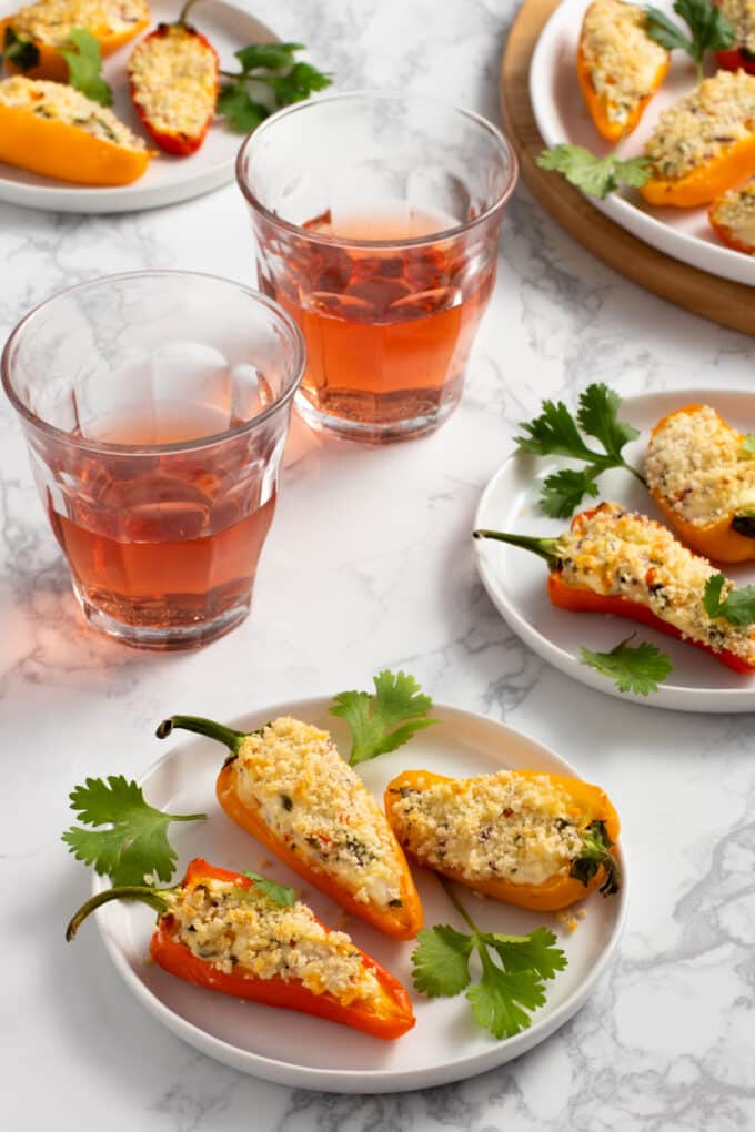 Halved baby bell peppers stuffed with cheese and topped with breadcrumbs, alongside glasses of rose.