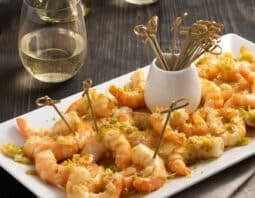 Shrimp Scampi Appetizer served with small skewers on a white platter, white wine in background.