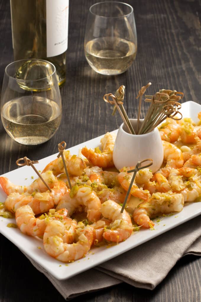 Shrimp Scampi Appetizer served with small skewers on a white platter, white wine in background.