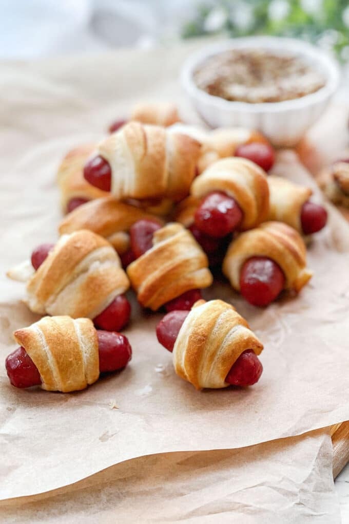 Pigs in a Blanket on parchment paper with a bowl of mustard in background.