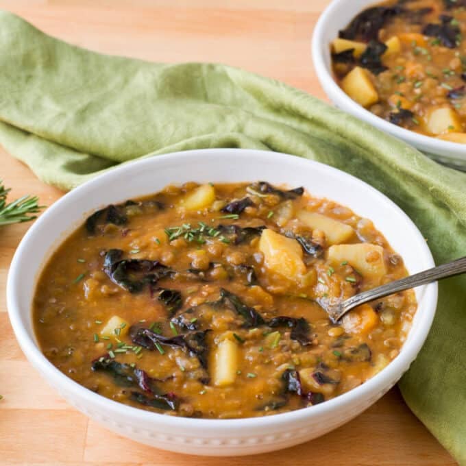 Lentil soup with potatoes and chard in white bowl.