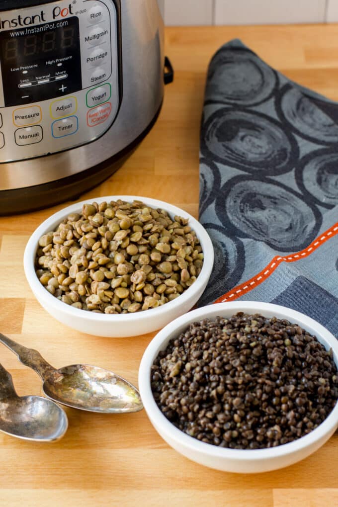 White bowls of cooked lentils in front of an instant pot.