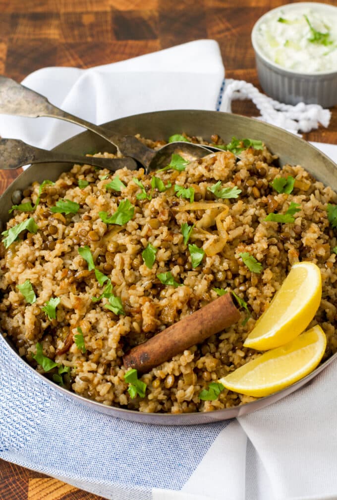 Rice, lentils, and caramelized onions in a pan with cinnamon stick and lemon wedges.