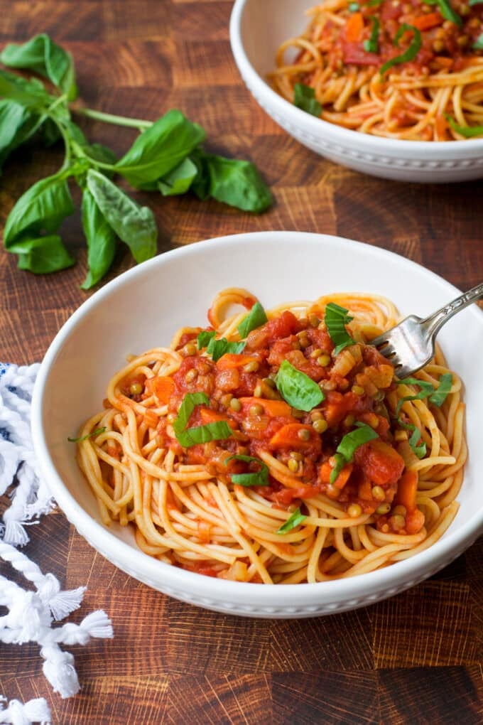 Lentil bolognese with spaghetti in a white bowl with fork.