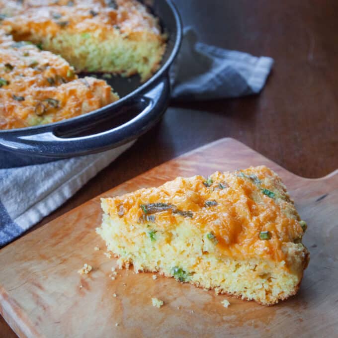 Slice of cheesy jalapeno cornbread in front of skillet.