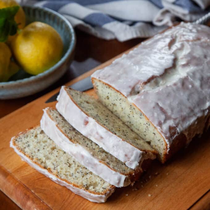 Glazed lemon poppy seed loaf with several slices cut.