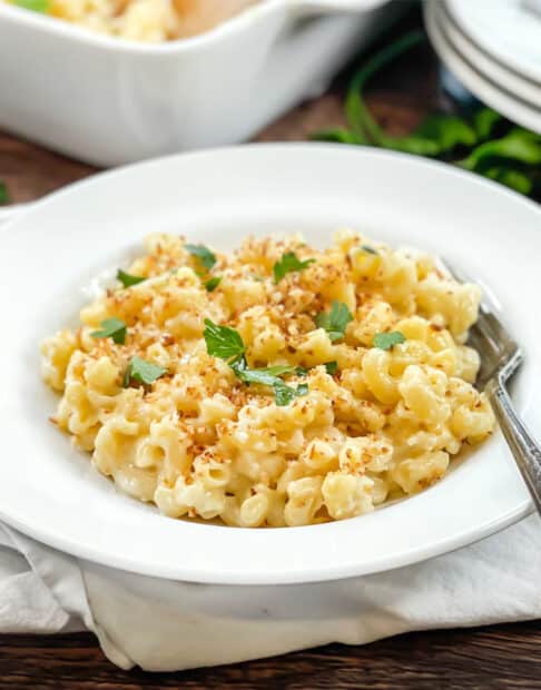 White dish of macaroni and cheese topped with breadcrumbs and parsley.