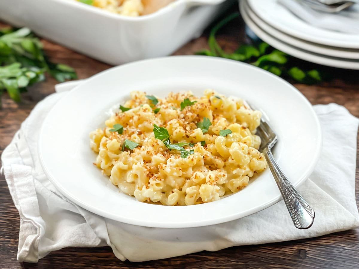 White dish of macaroni and cheese topped with breadcrumbs and parsley.