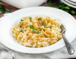 White dish of macaroni and cheese topped with breadcrumbs and parsley.
