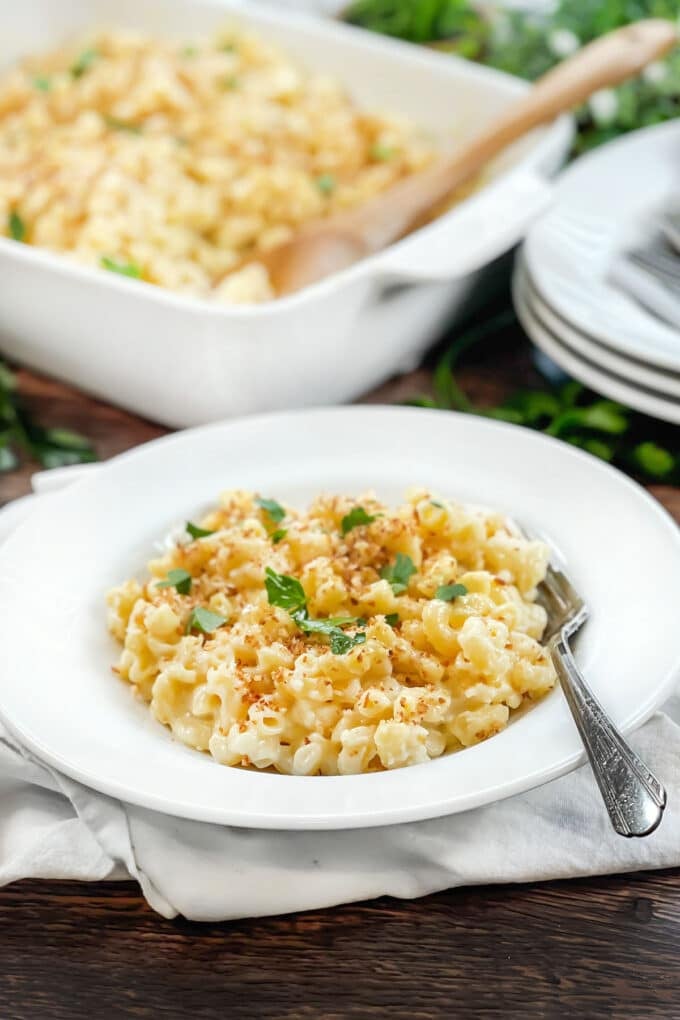 White dish of macaroni and cheese topped with breadcrumbs and parsley.