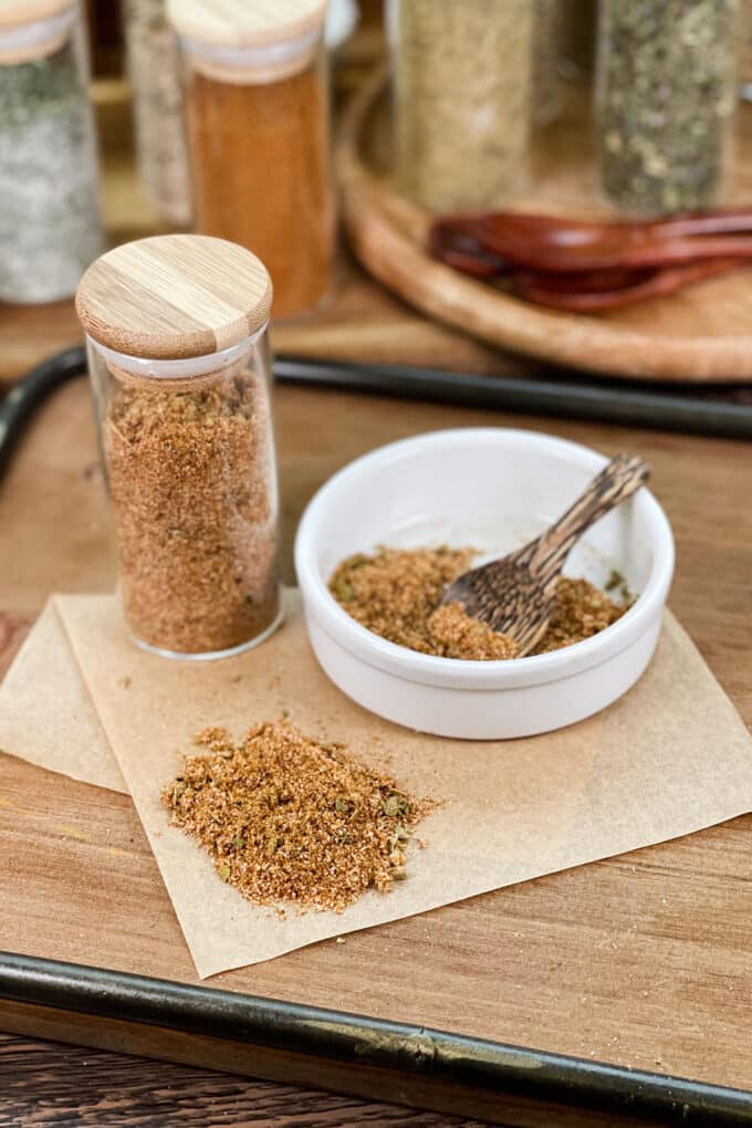 Fajita seasoning blend in a glass jar, as well as in a white dish with small wood spoon.