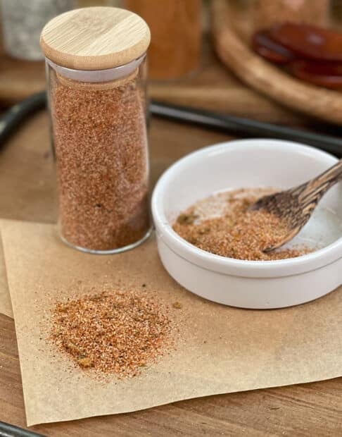 Taco seasoning blend in glass jar, white dish with tiny wooden spoon.