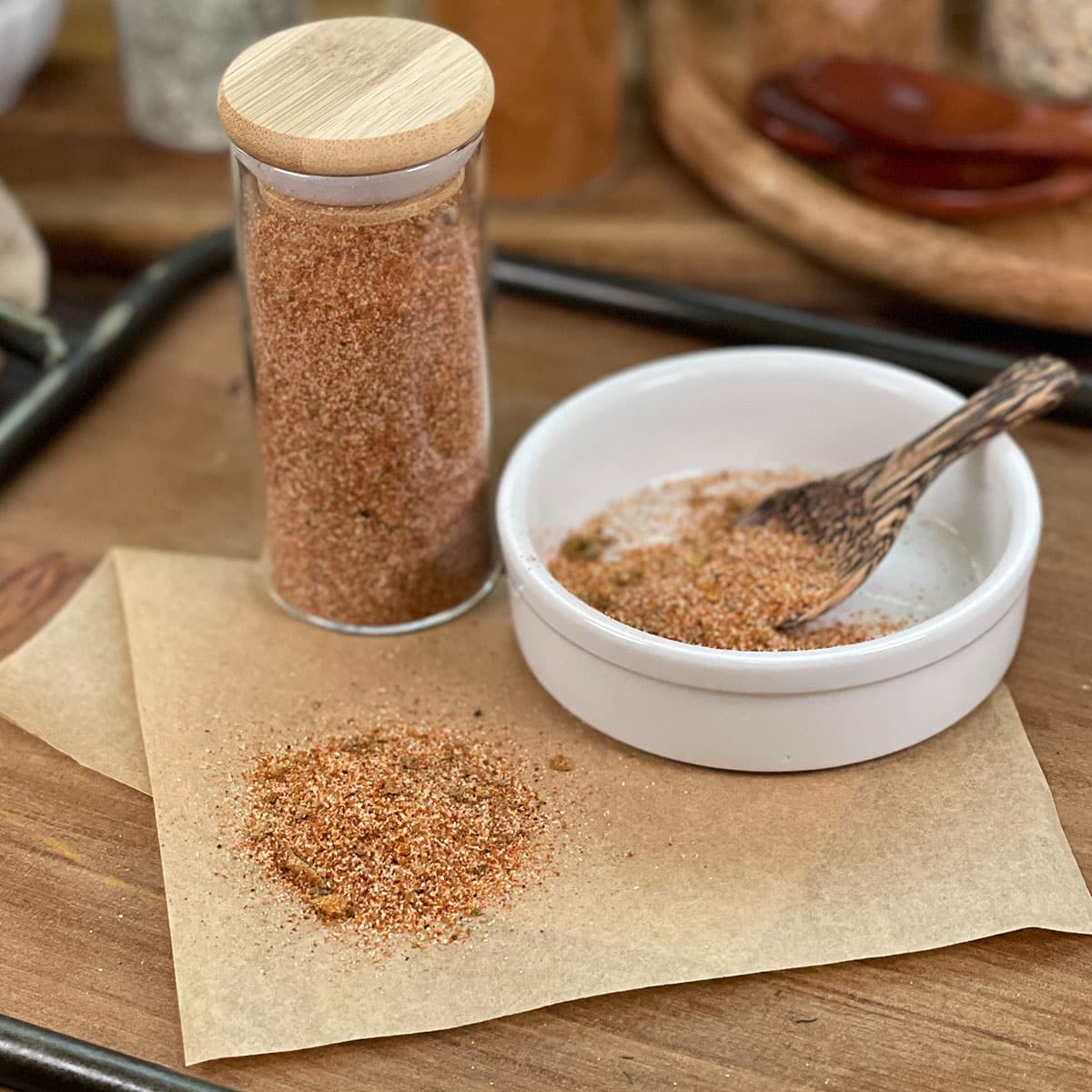 Taco seasoning blend in glass jar, white dish with tiny wooden spoon.