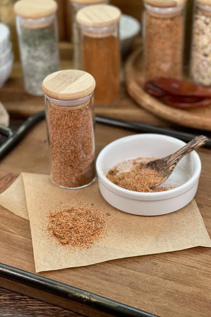 Taco seasoning blend in glass jar, white dish with tiny wooden spoon.