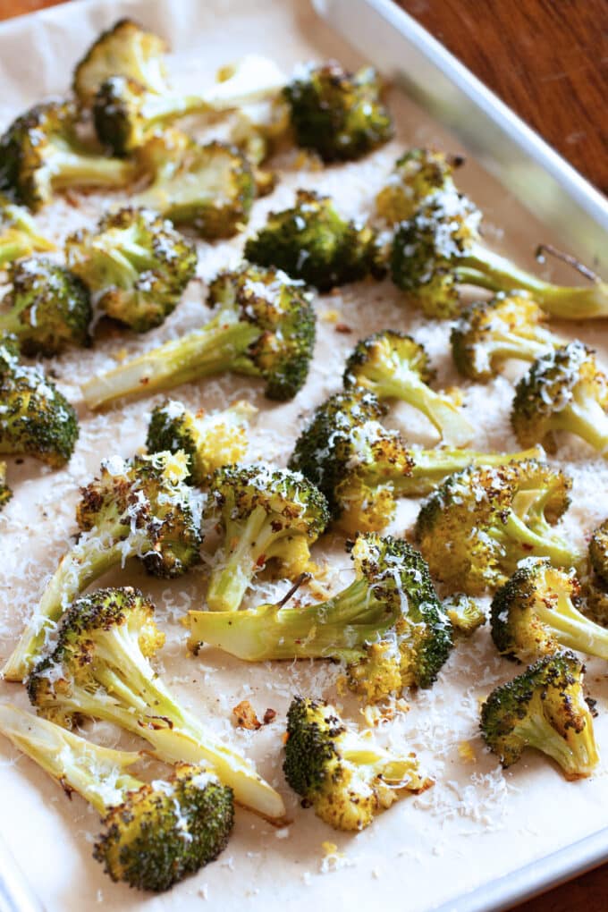 Roasted broccoli with lemon zest and Parmesan on a parchment lined baking sheet.
