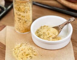 Homemade Adobo seasoning in glass jar, in dish with spoon, and spilled on parchment paper.
