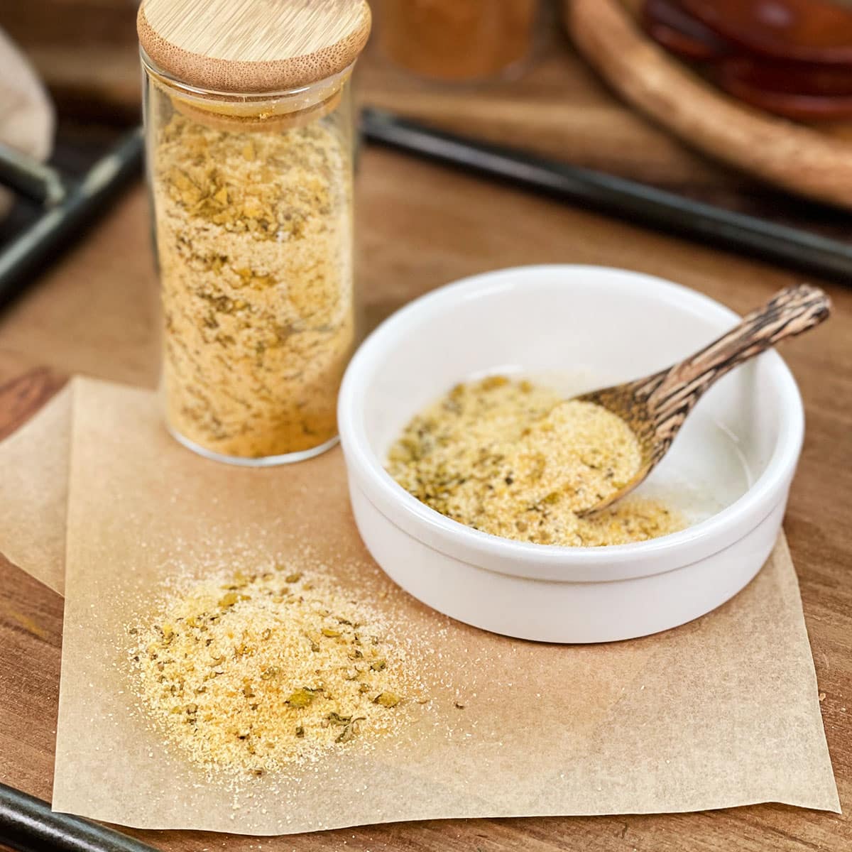 Homemade Adobo seasoning in glass jar, in dish with spoon, and spilled on parchment paper.